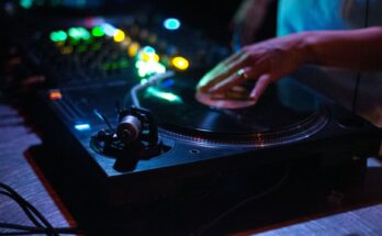 Hand die een vinylplaat bedient op een draaitafel in kleurrijk clublicht