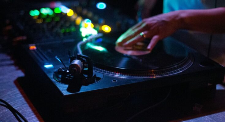 Hand die een vinylplaat bedient op een draaitafel in kleurrijk clublicht