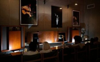 Donkere luisterbar met publiek, luidsprekers en muziekposters aan de wand