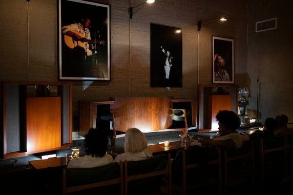 Donkere luisterbar met publiek, luidsprekers en muziekposters aan de wand